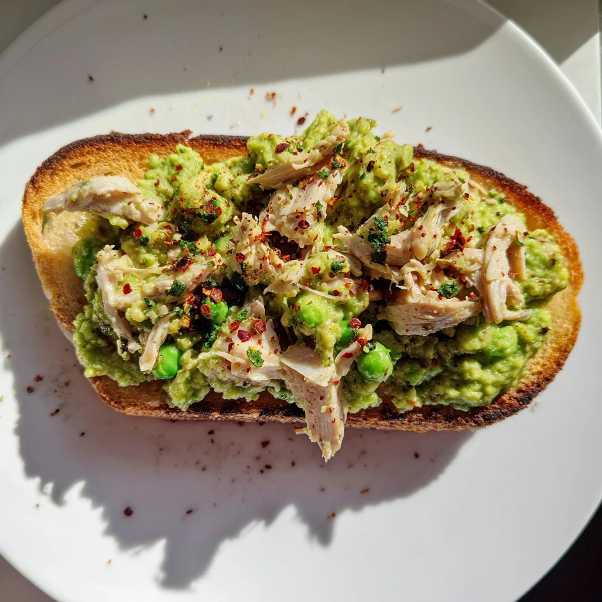 Smashed pea and chicken toast features creamy mashed peas and shredded chicken on golden, crisp rustic bread.