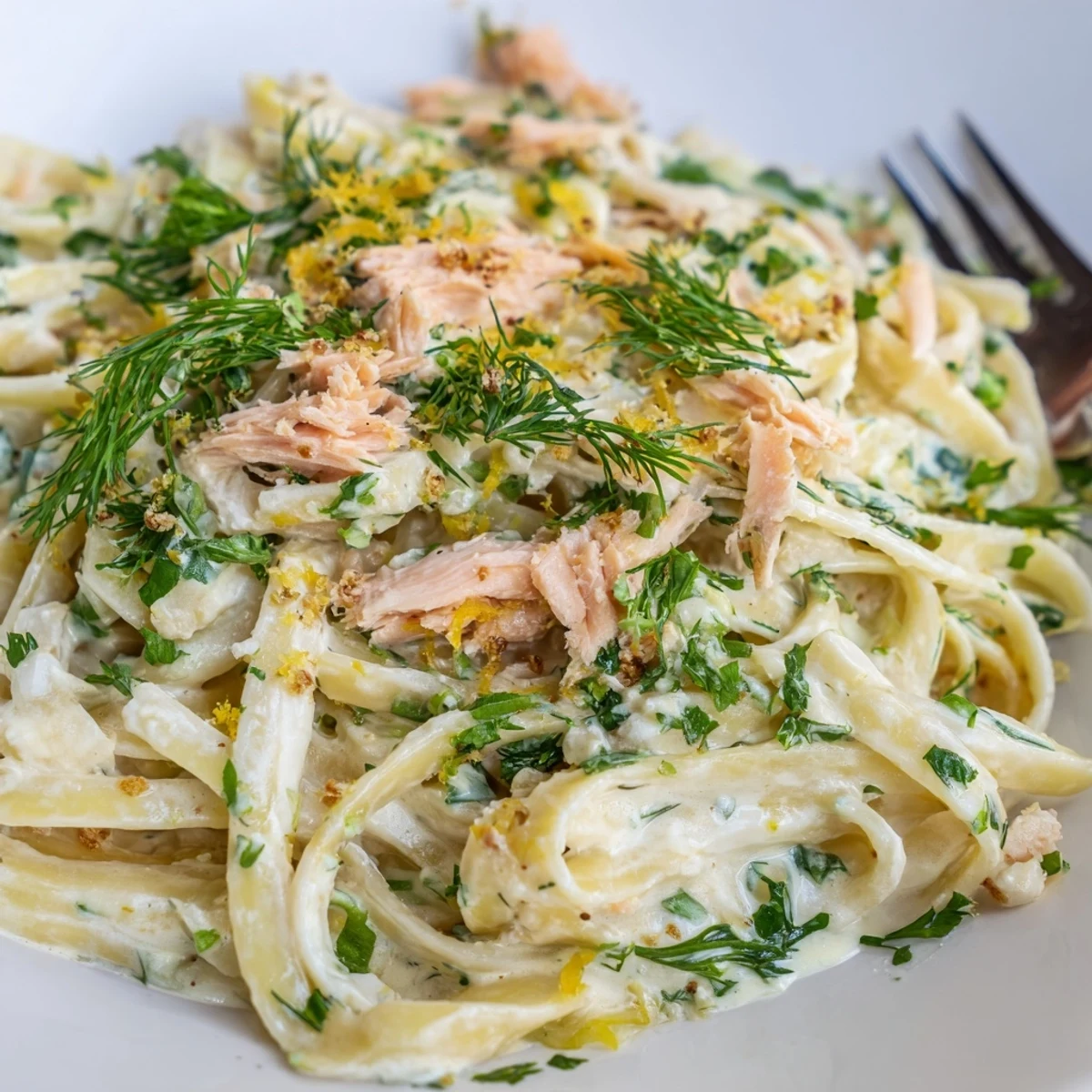 Creamy Salmon Pasta plated in a white bowl, flaked hot-smoked salmon and fresh dill atop fettuccine, lemon wedges on the side.