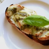 A sliced Pesto Chicken Melt reveals layers of basil pesto, tender chicken, and fresh tomato slices on a plate.  