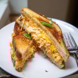 Buffalo Chicken Ranch Grilled Cheese is served halved on a white plate, garnished with fresh green onions for a colorful, appetizing finish.  