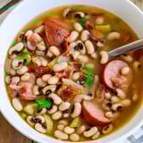 A rustic bowl of Southern-Style Black-Eyed Peas served with smoky sausage and cornbread on the side.  