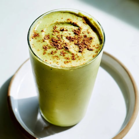 A vibrant Matcha Eggnog Collagen Breakfast Smoothie topped with a sprinkle of fragrant nutmeg.