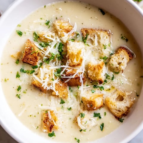 A steaming bowl of Creamy Garlic Bread Soup, topped with fresh parsley, looks unbelievably delicious.