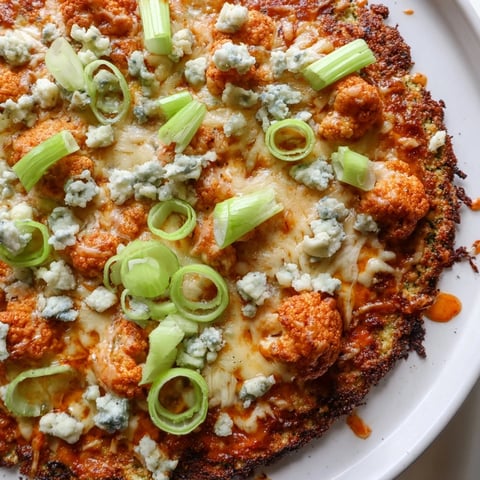 A golden, crispy Buffalo Cauliflower Pizza slice shows spicy red sauce and melted mozzarella on a rustic wooden cutting board.  