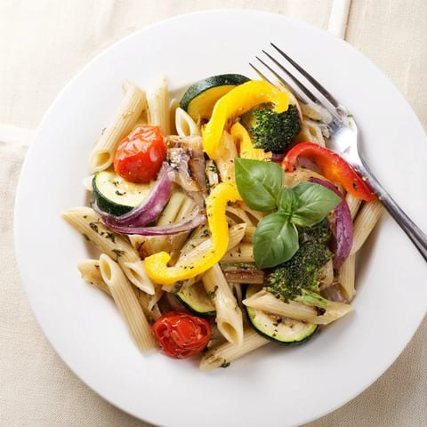 A close-up of vibrant Pasta Primavera, showcasing roasted zucchini, bell peppers, and cherry tomatoes tossed with al dente pasta and fresh basil.