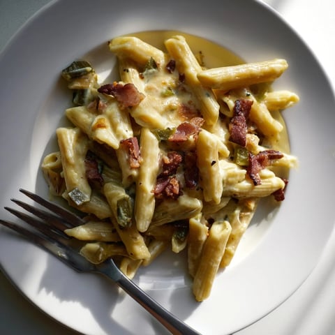 Creamy Jalapeño Popper Pasta is plated with crispy bacon bits, charred jalapeño slices, and a golden breadcrumb topping for a spicy, cheesy comfort meal.