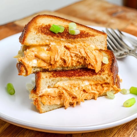A close-up of Buffalo Chicken Ranch Grilled Cheese oozing melted sharp cheddar and spicy buffalo chicken between golden, buttery sourdough slices.  