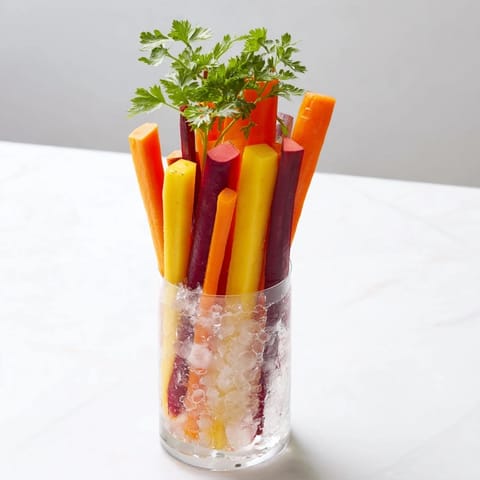 Vibrant rainbow carrot sticks chilled in tall glasses, a refreshing crudités appetizer at a party.