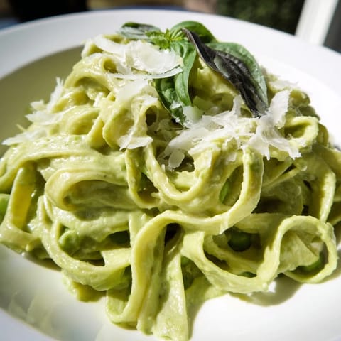 A bowl of Creamy Green Pea Alfredo, featuring fettuccine coated in a velvety green sauce, garnished with fresh basil and grated Parmesan.