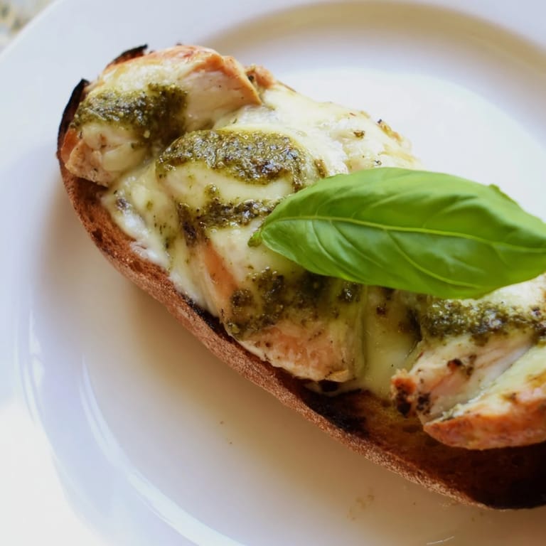 A sliced Pesto Chicken Melt reveals layers of basil pesto, tender chicken, and fresh tomato slices on a plate.  